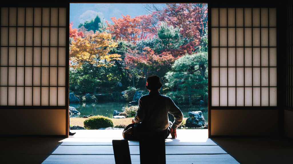 Personne assise dans une pièce traditionnelle japonaise regardant un jardin zen à travers une grande ouverture